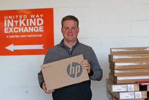 a principal holds a stack of chromebooks donated to an all in for youth school