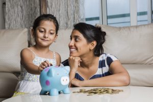 Mother and daughter putting coins into piggy bank - Stock image