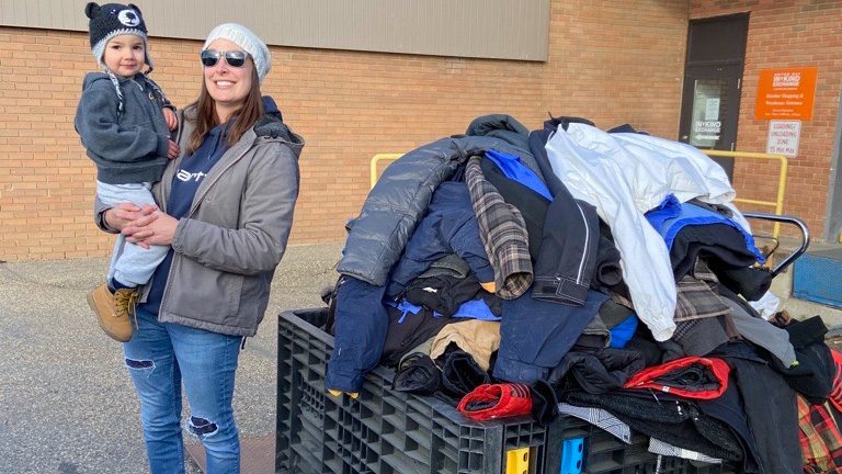 A woman and child stand next to a pile of coats at the United Way In Kind Exchange. They volunteered by hosting a coat drive to support Coats for Kids and Families,