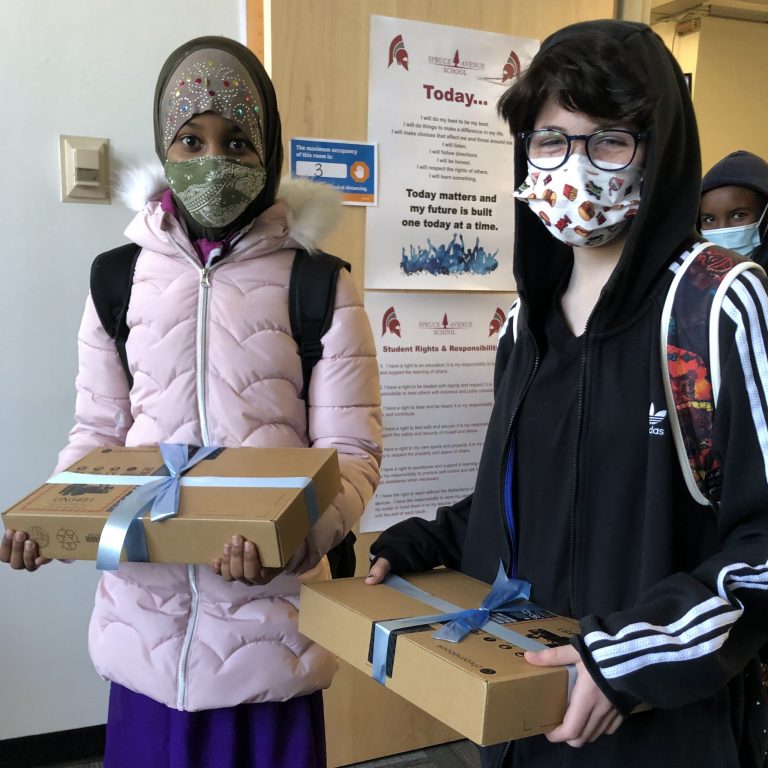 Two students hold gift wrapped Chromebooks and smile