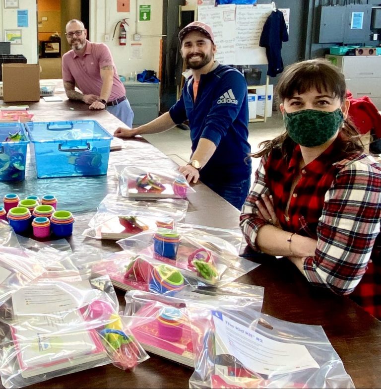 Three staff members smile while packing up supplies for Kid Kits