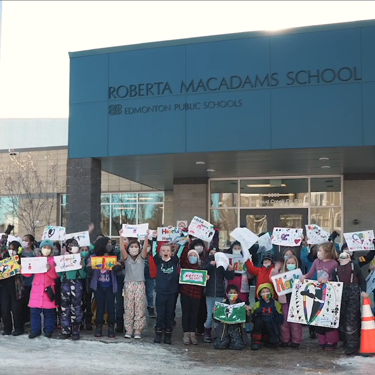 Students from Roberta MacAdams school raise hand drawn signs of encouragement