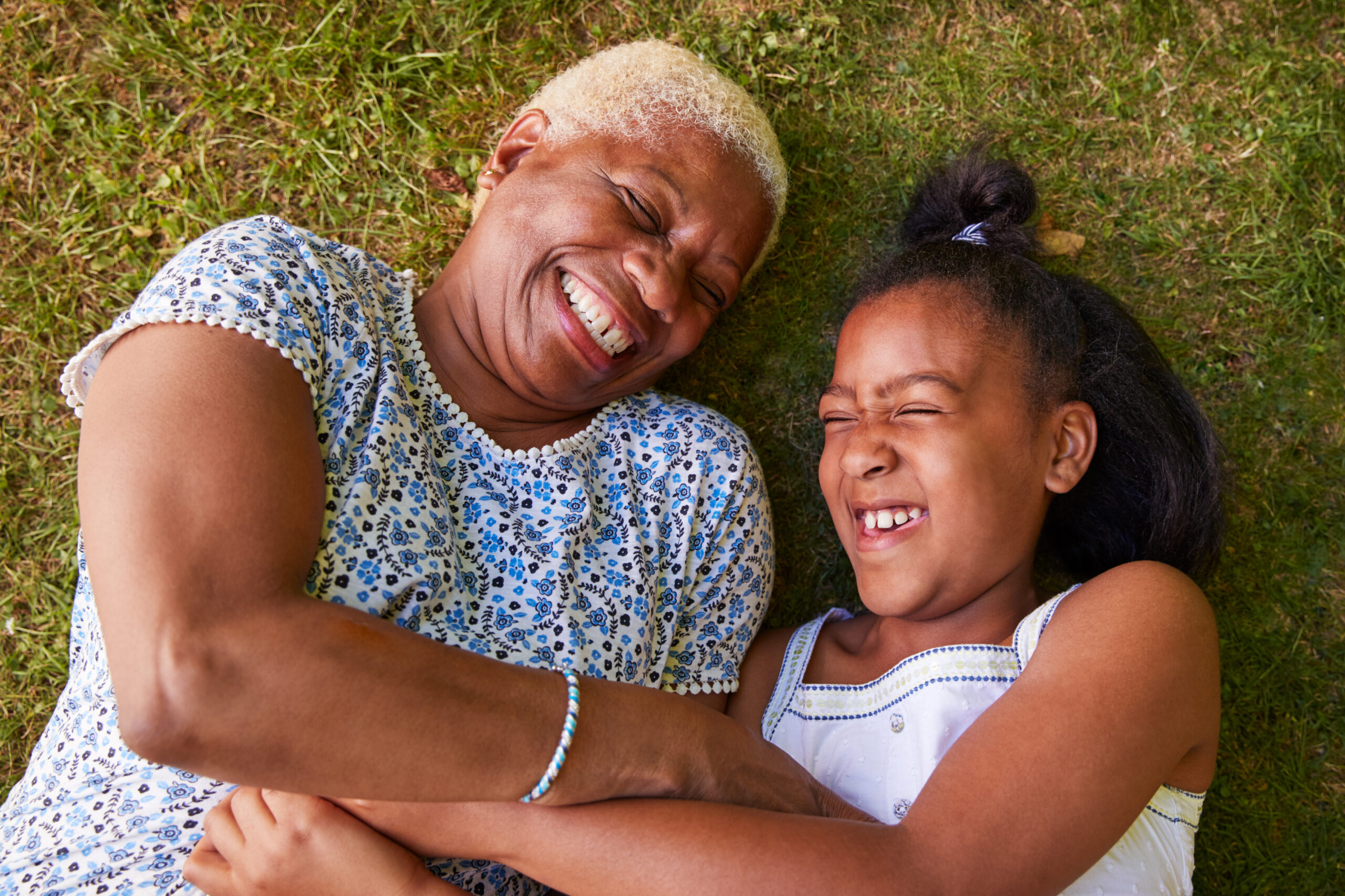 Black girl and grandmother lying on grass, overhead close up