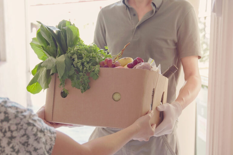 Man wearing gloves home delivering food box, volunteer holding grocery box for donation, supporting local business concept