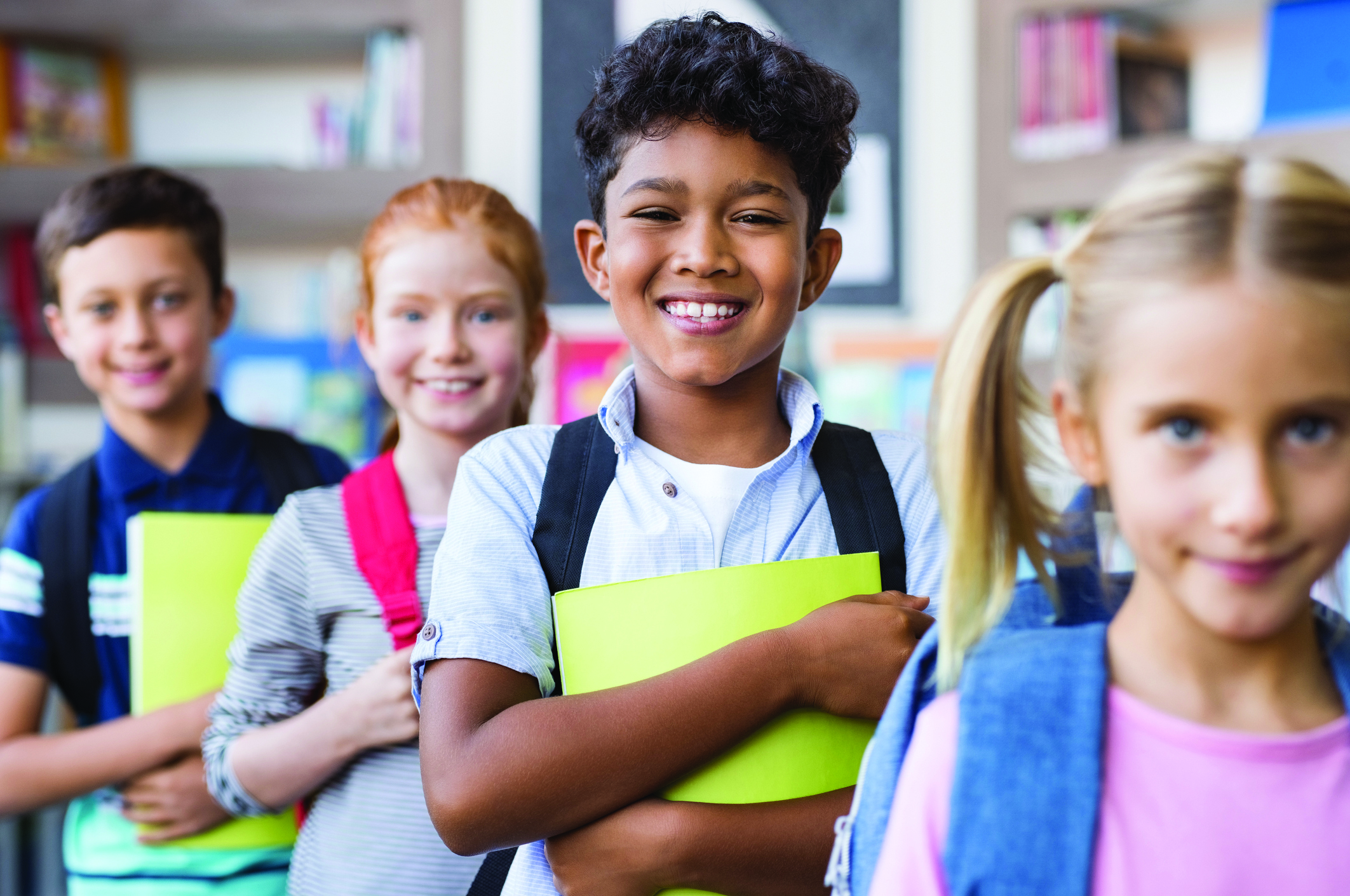 Portrait of happy multiethnic children holding books and wearing backpack at primary school.