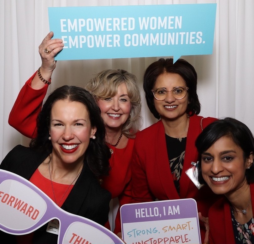 Four smiling women pose with props at the Women United Compassion in Command photo booth.