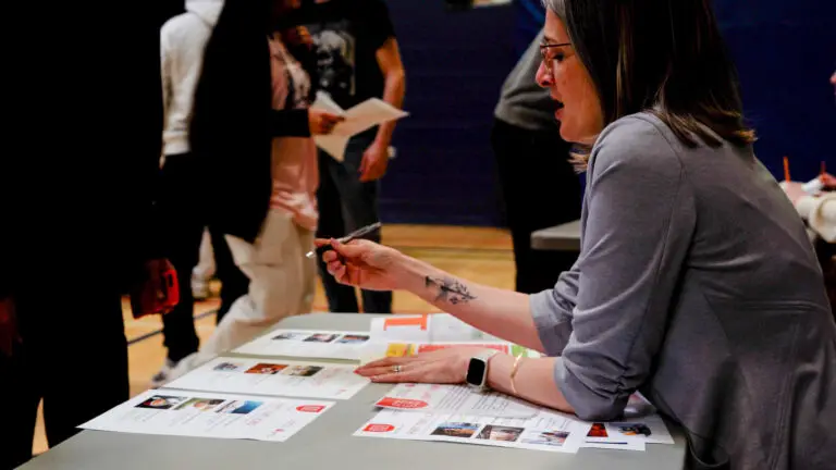 A female volunteer explains options to students at a sales booth during Financial Reality Check.