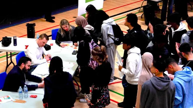 A large group of high school students line up at a booth during the Financial Reality Check simulation held in their school's gymnasium.