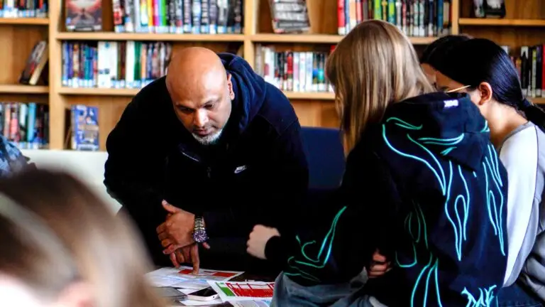 A male volunteer helps students calculate their budgets in a school library at the Financial Reality Check simulation.